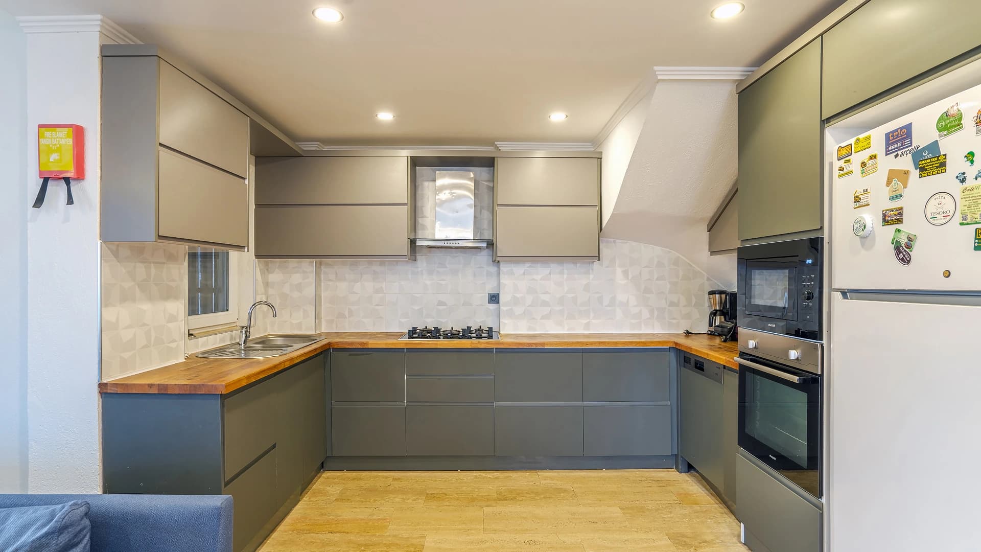Modern kitchen with olive-green cabinetry, wood countertops, and stainless steel appliances.