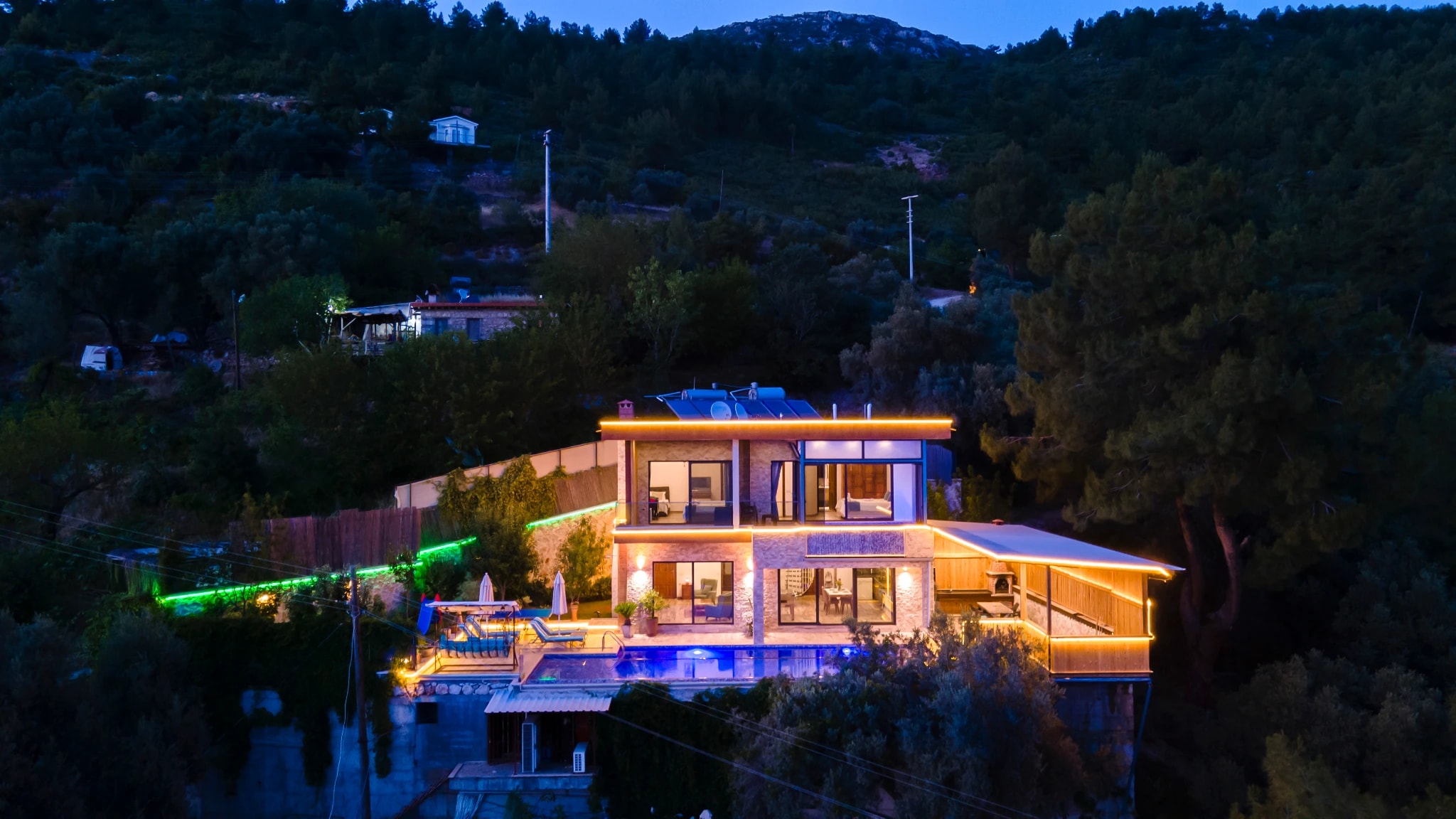 Stunning nighttime exterior view of the modern villa with illuminated infinity pool and mountain backdrop.