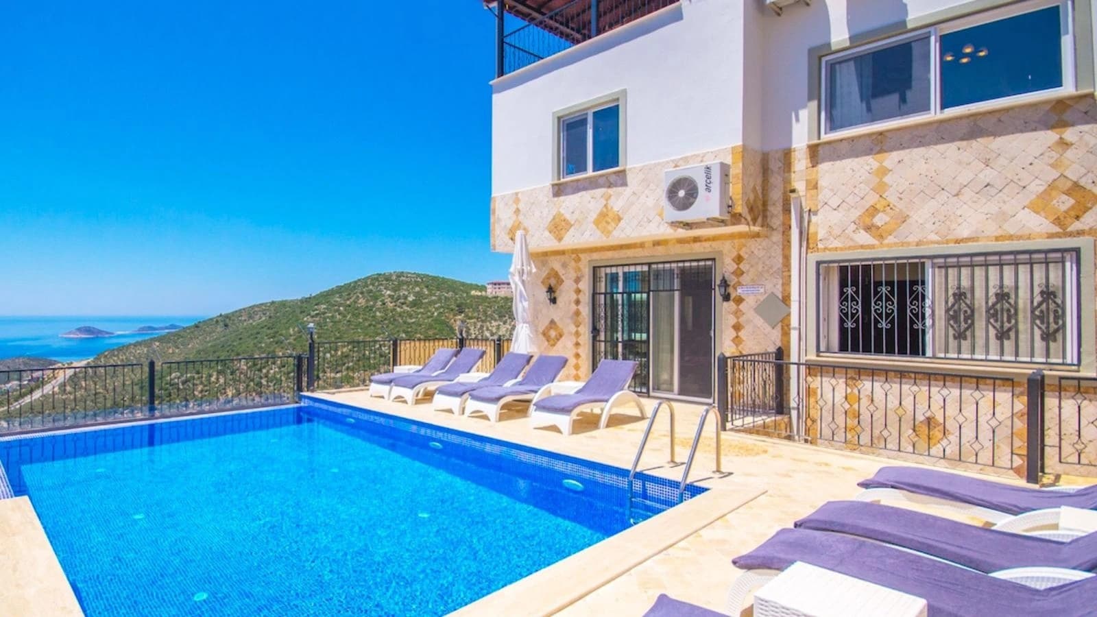 Sparkling infinity-style pool with purple loungers overlooking scenic coastal landscape.