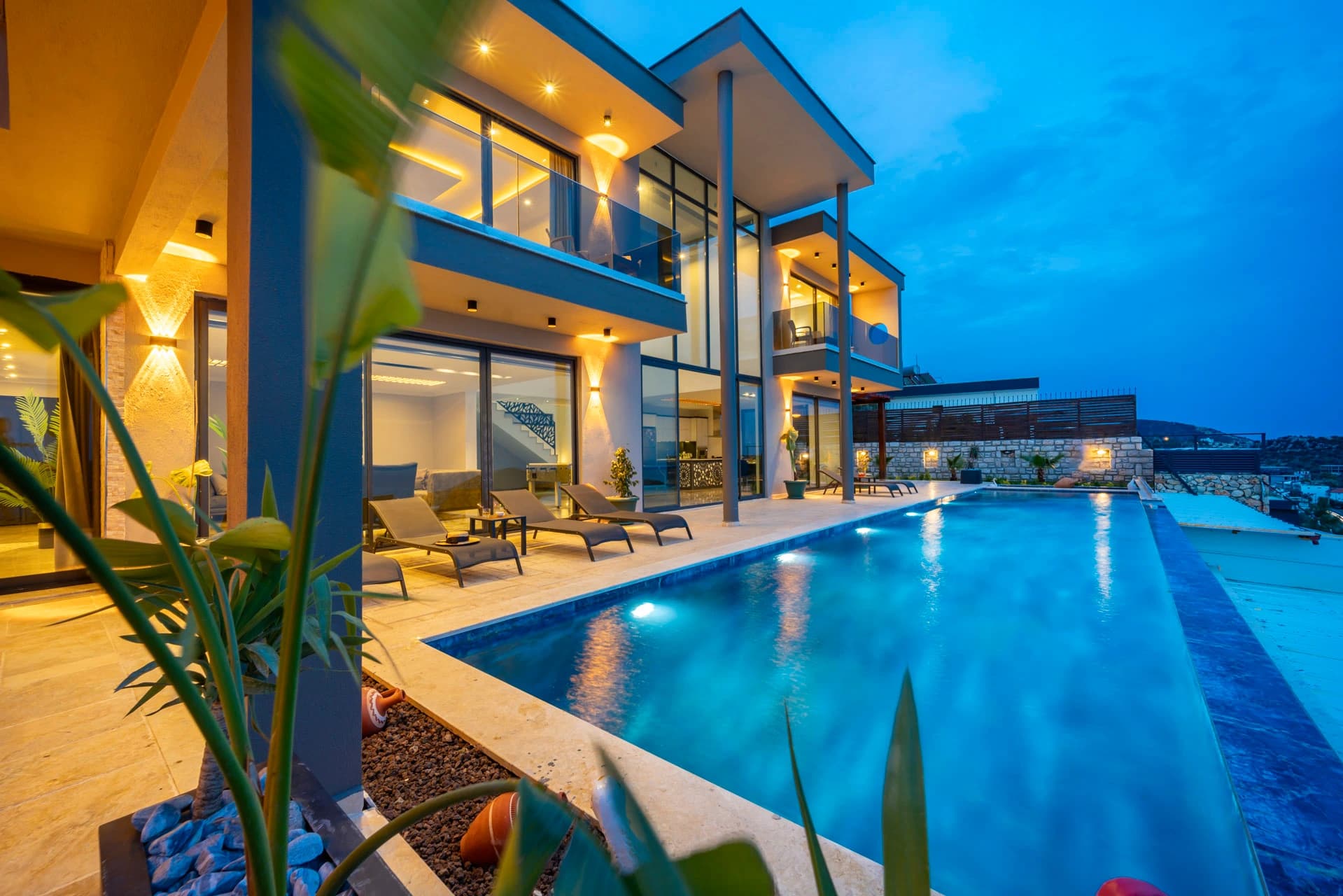 Luxurious infinity pool at night with villa and terrace seating overlooking coastal views.