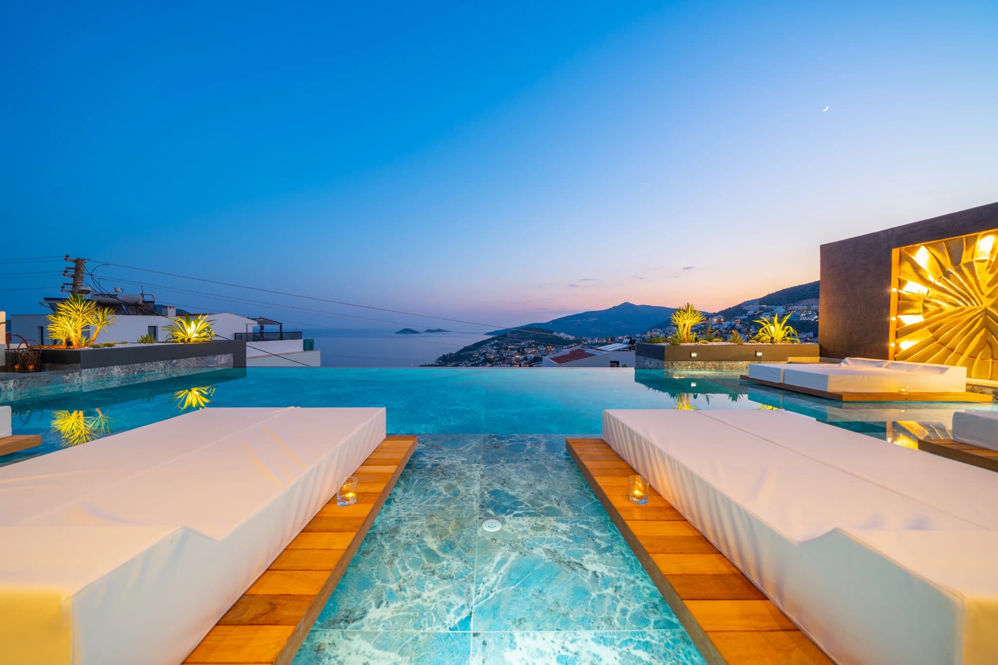 Illuminated infinity pool framing panoramic coastal and mountain scenery.
