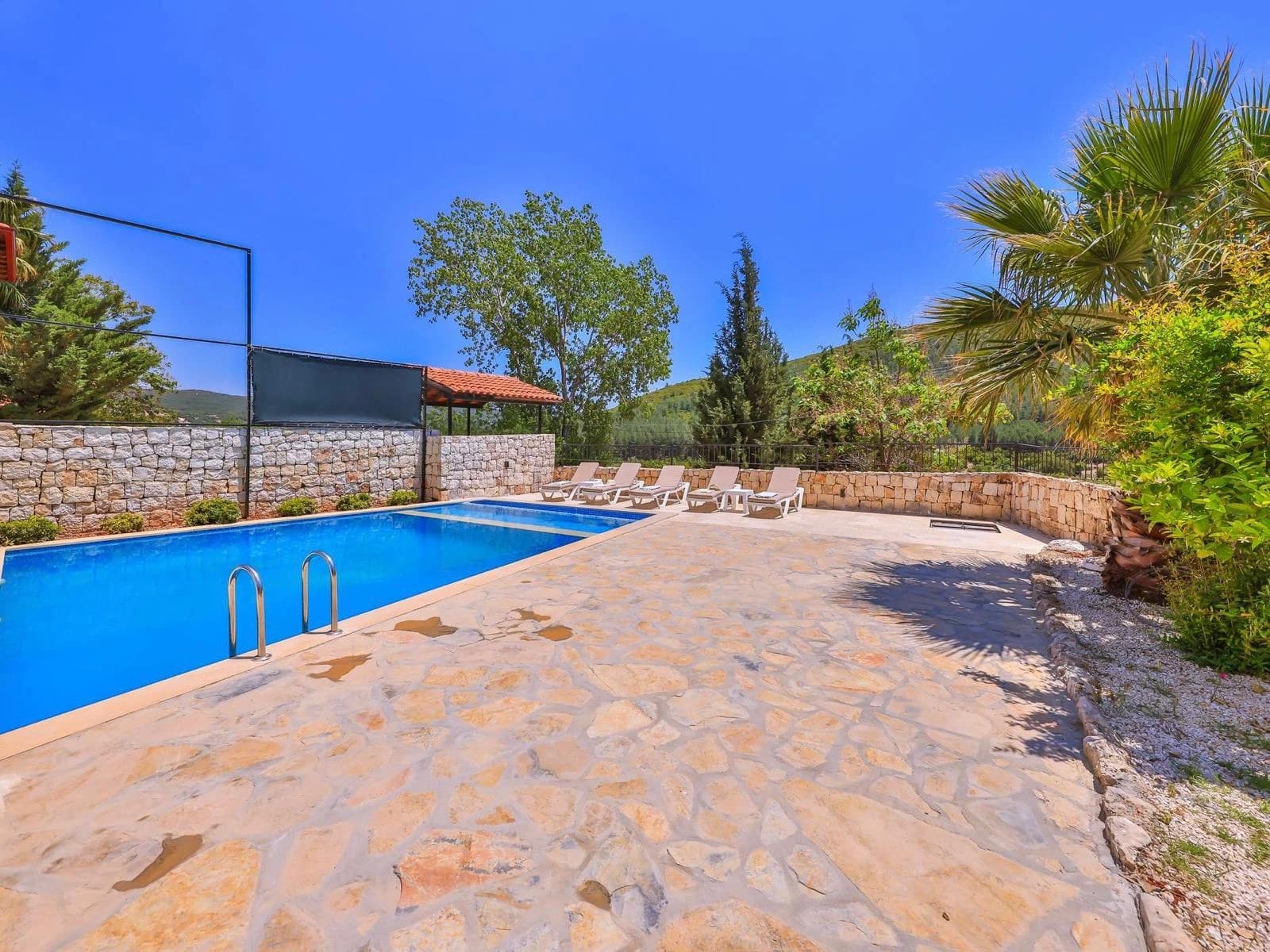 Ground-level view of the sparkling blue pool with comfortable sun loungers and garden.
