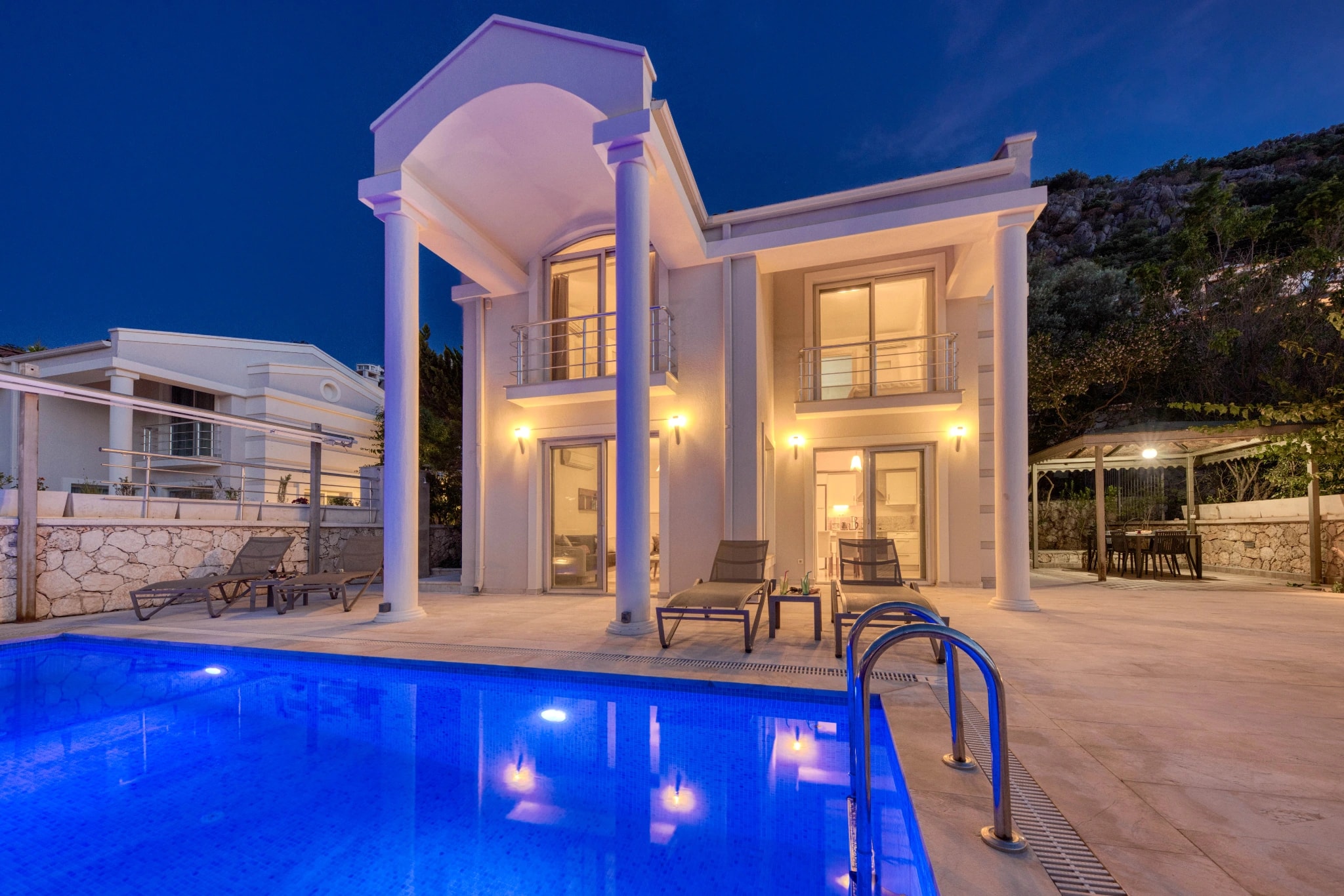 Illuminated private pool fronting contemporary villa at twilight.