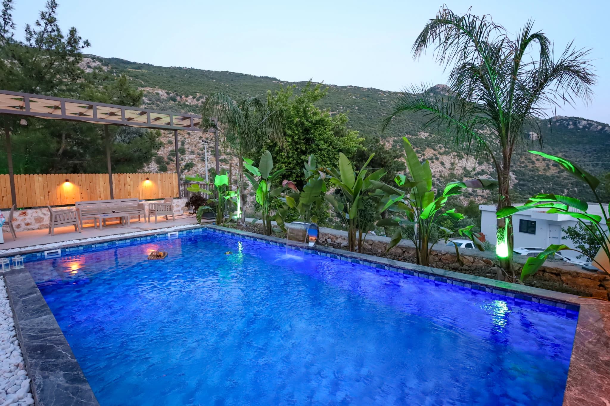 Night-time pool view with mountain backdrop and lush tropical vegetation.