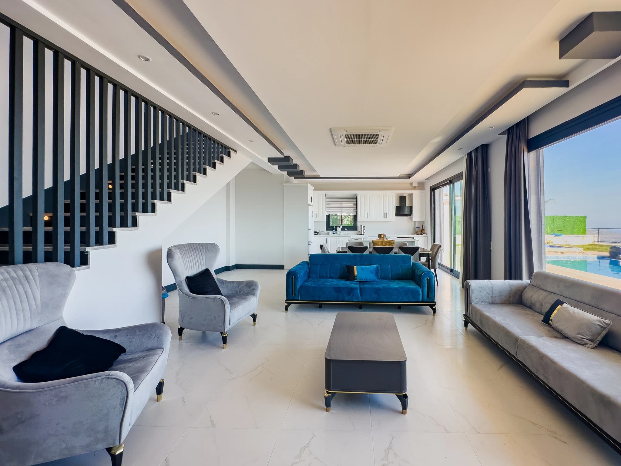 Spacious open-plan living room with multiple seating areas, modern furnishings, and views toward the pool and sea.