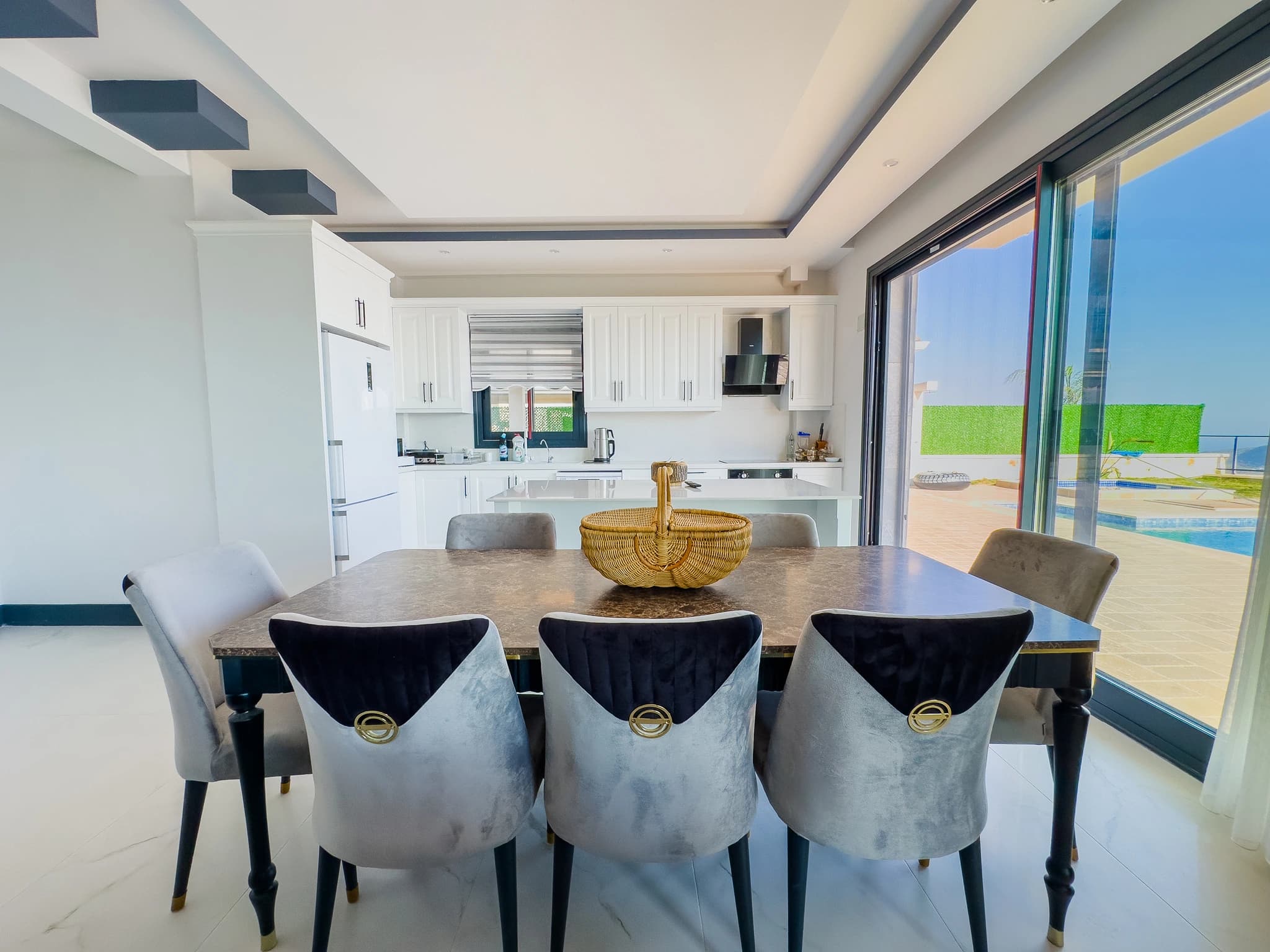 Dining area adjacent to white kitchen with pool views through sliding glass doors.