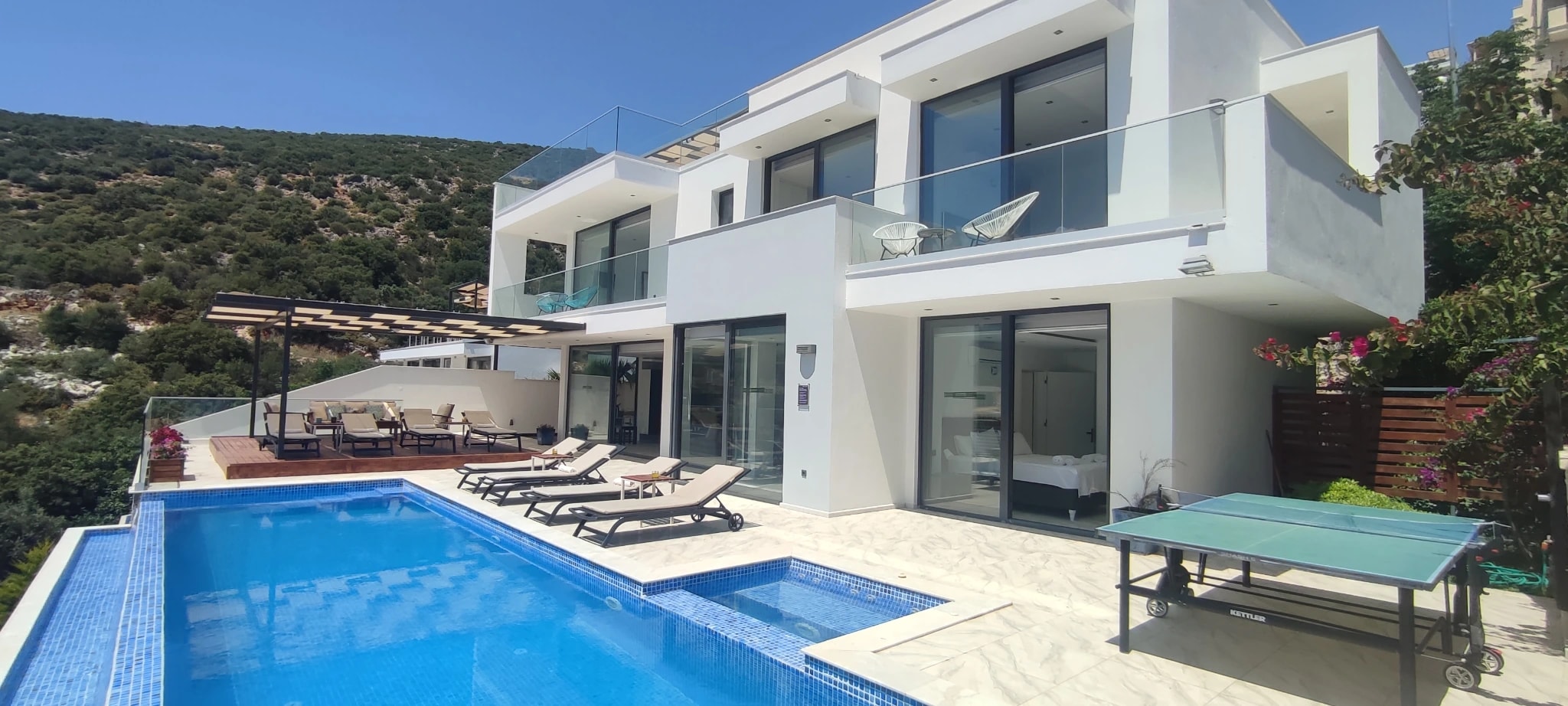 Villa exterior with private pool, sun loungers, table tennis table, and lush mountain setting.