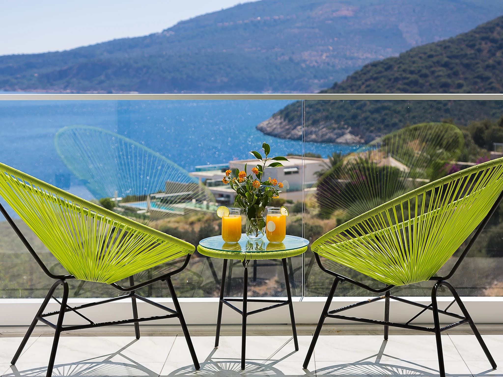 Stunning balcony terrace with lime-green lounge chairs overlooking sea, mountains, and infinity pool.