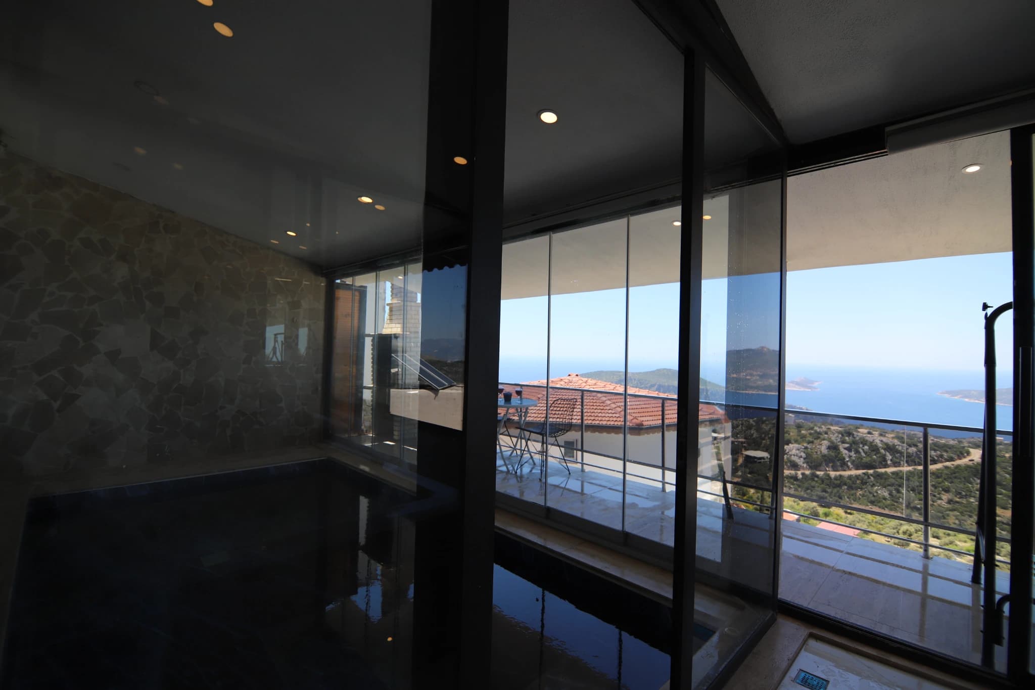 Interior view of expansive sea and mountain landscape through floor-to-ceiling windows.