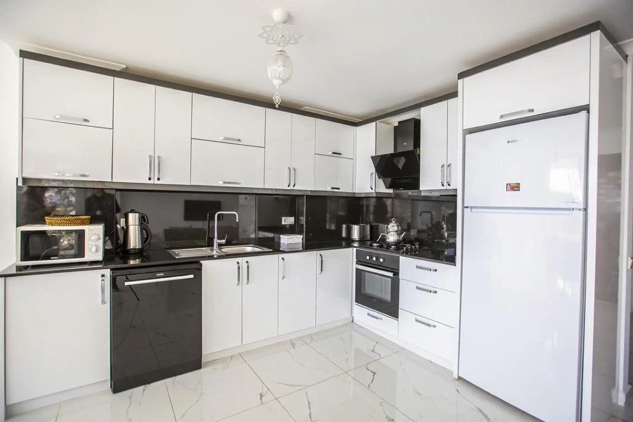 Contemporary kitchen with white cabinetry, black backsplash, and stainless steel appliances.