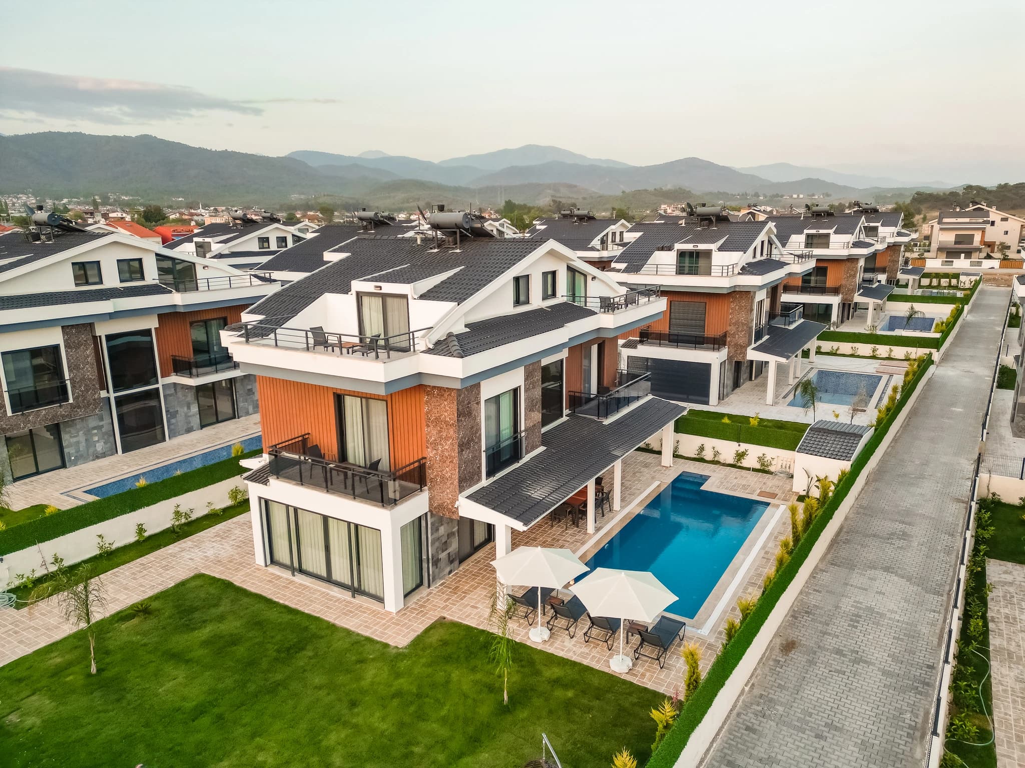 Bird's-eye view of modern villa complex with multiple private pools and organized parking layout.