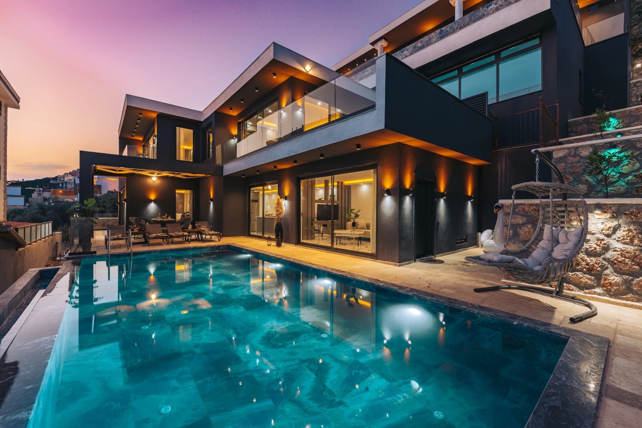 Beautifully lit private pool at dusk with modern villa and comfortable lounging areas.