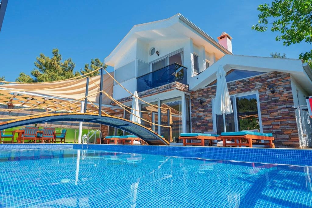 Contemporary villa exterior with blue-tiled pool, multi-level terraces, and lush surroundings.