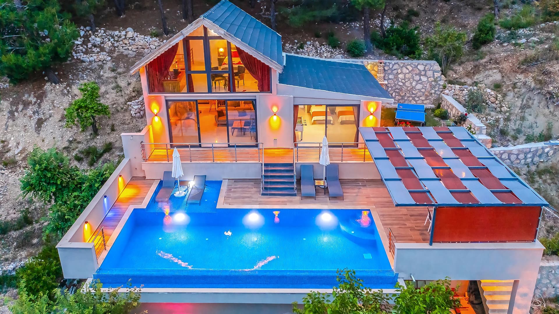 Illuminated private swimming pool with surrounding terrace and outdoor lounge area.