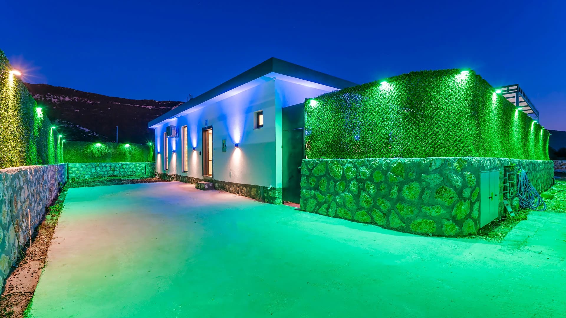 Modern villa exterior illuminated at dusk with striking green hedge landscaping and contemporary architecture.