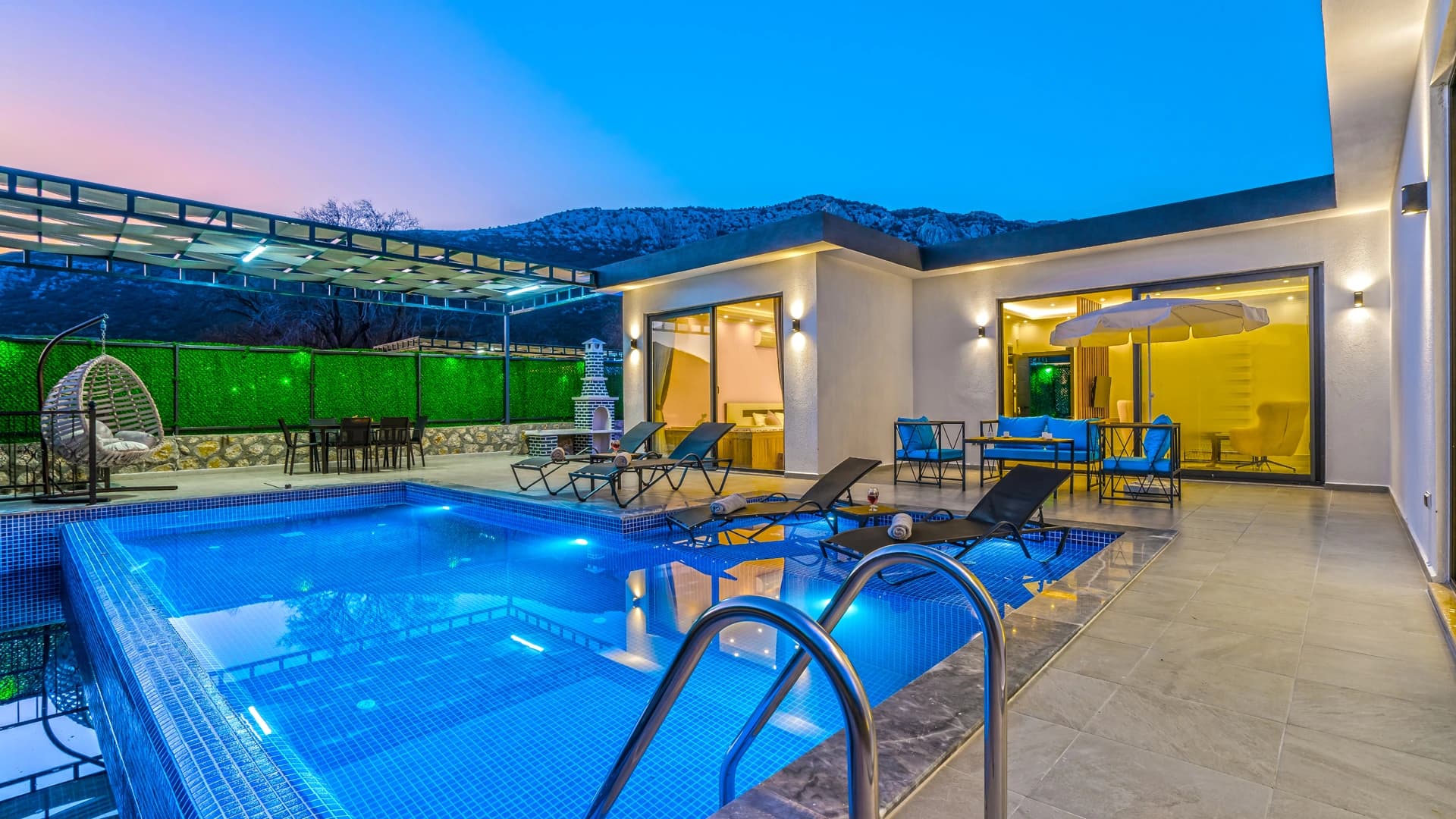 Stunning illuminated pool terrace with mountain backdrop and modern lounging areas at dusk.