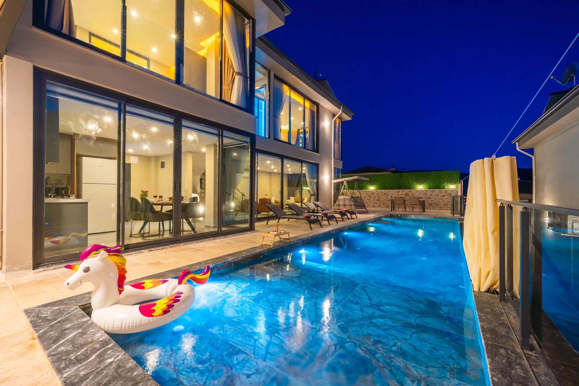 Illuminated private pool with loungers and modern villa facade.