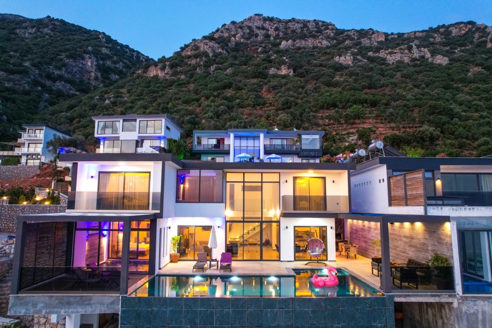Evening view of contemporary villa with lit pool and mountain backdrop.