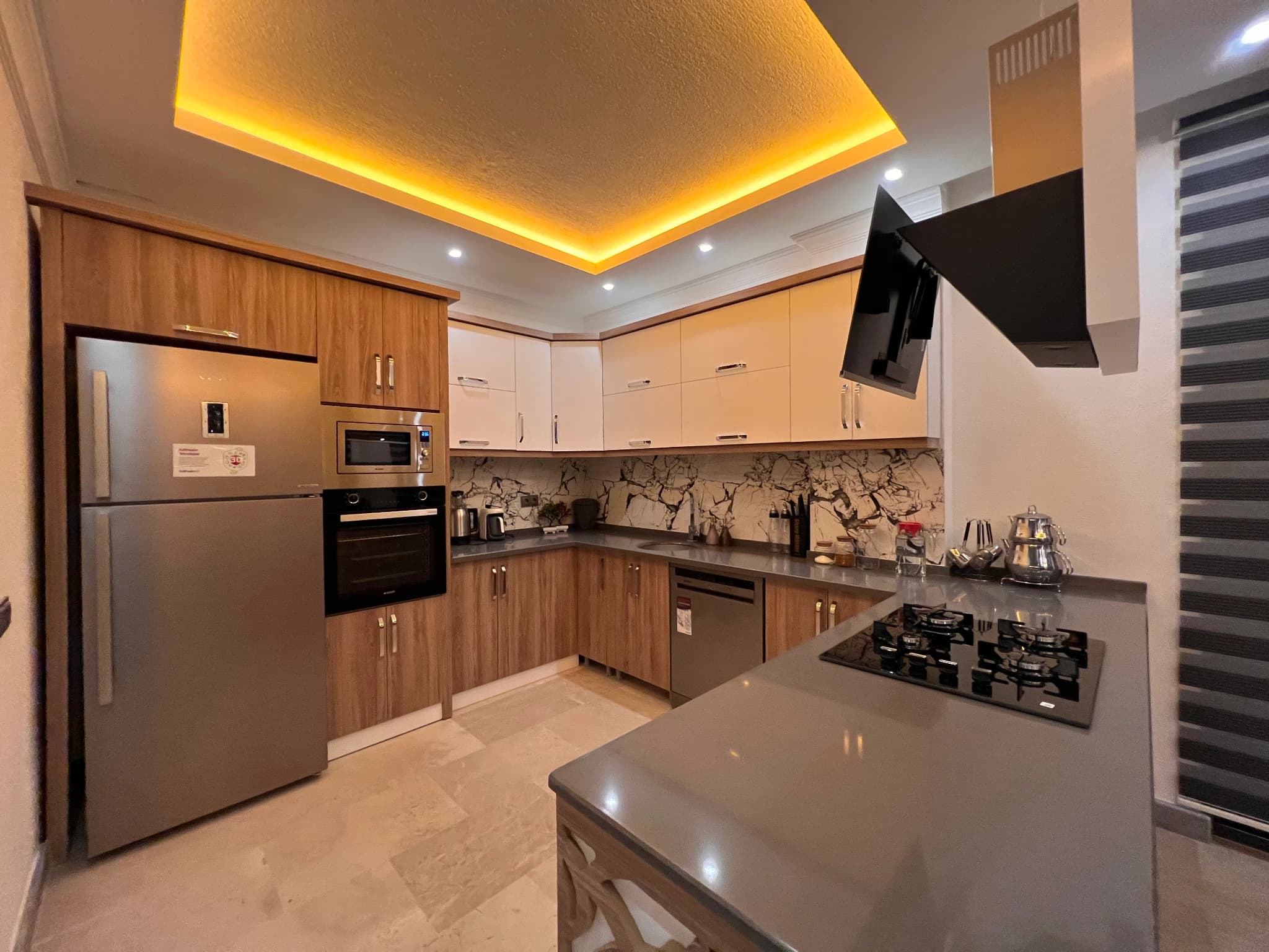 Modern fully-equipped kitchen with wood cabinetry, gas stove, and ambient ceiling lighting.