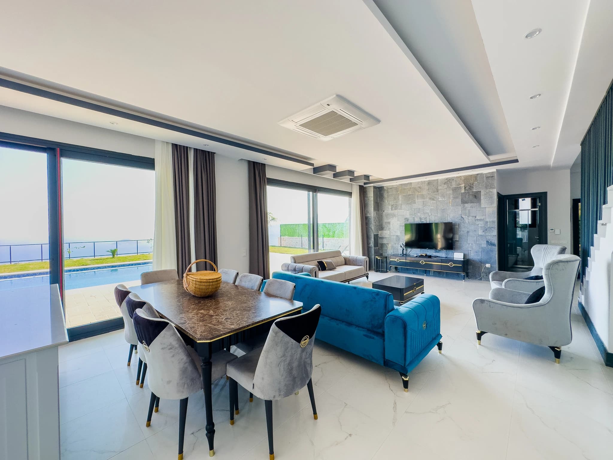 Modern open-concept dining and living area with marble table, elegant seating, and direct pool and sea views.