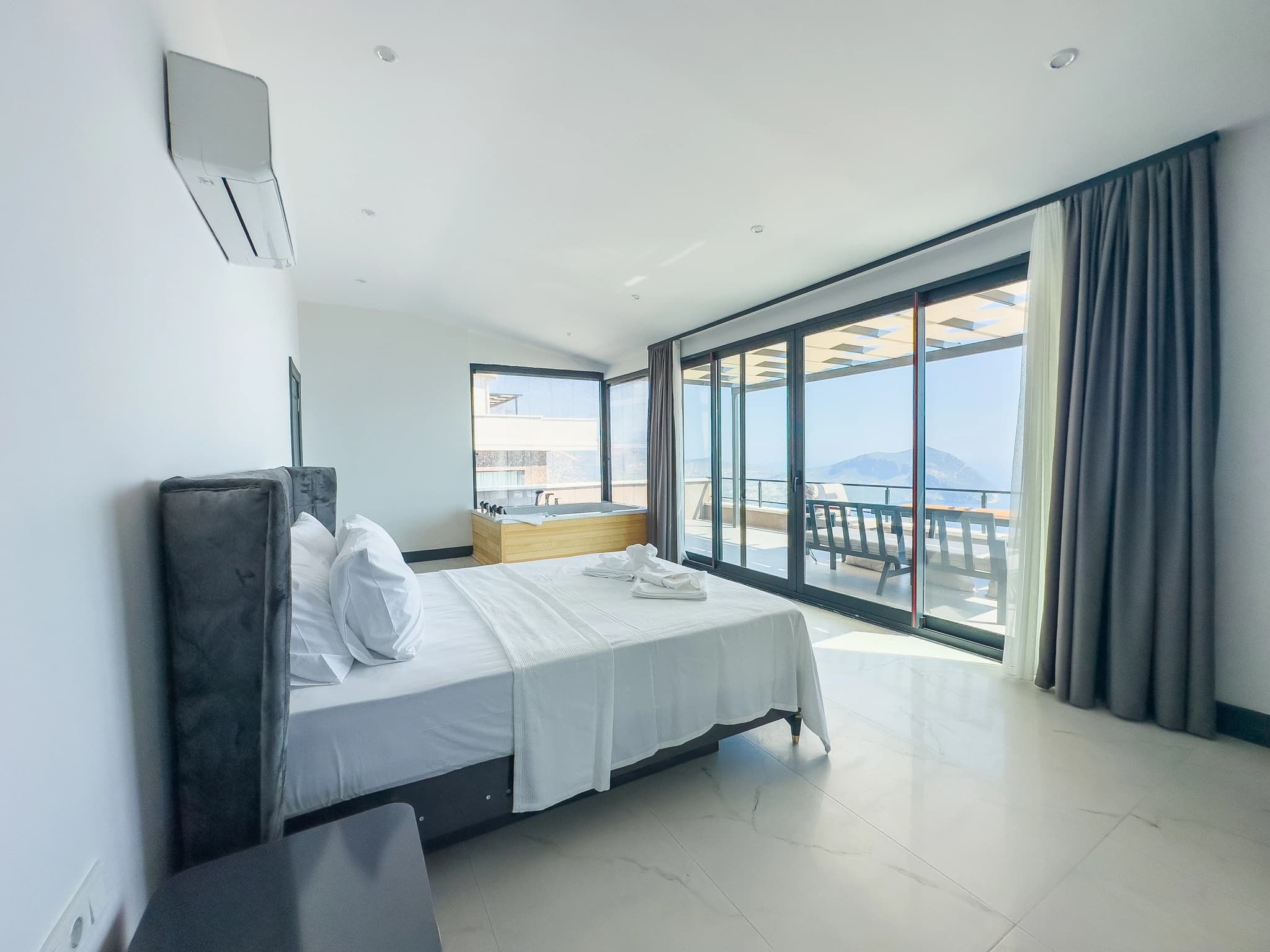 Bright bedroom with king bed, jacuzzi tub, and private balcony overlooking the sea.