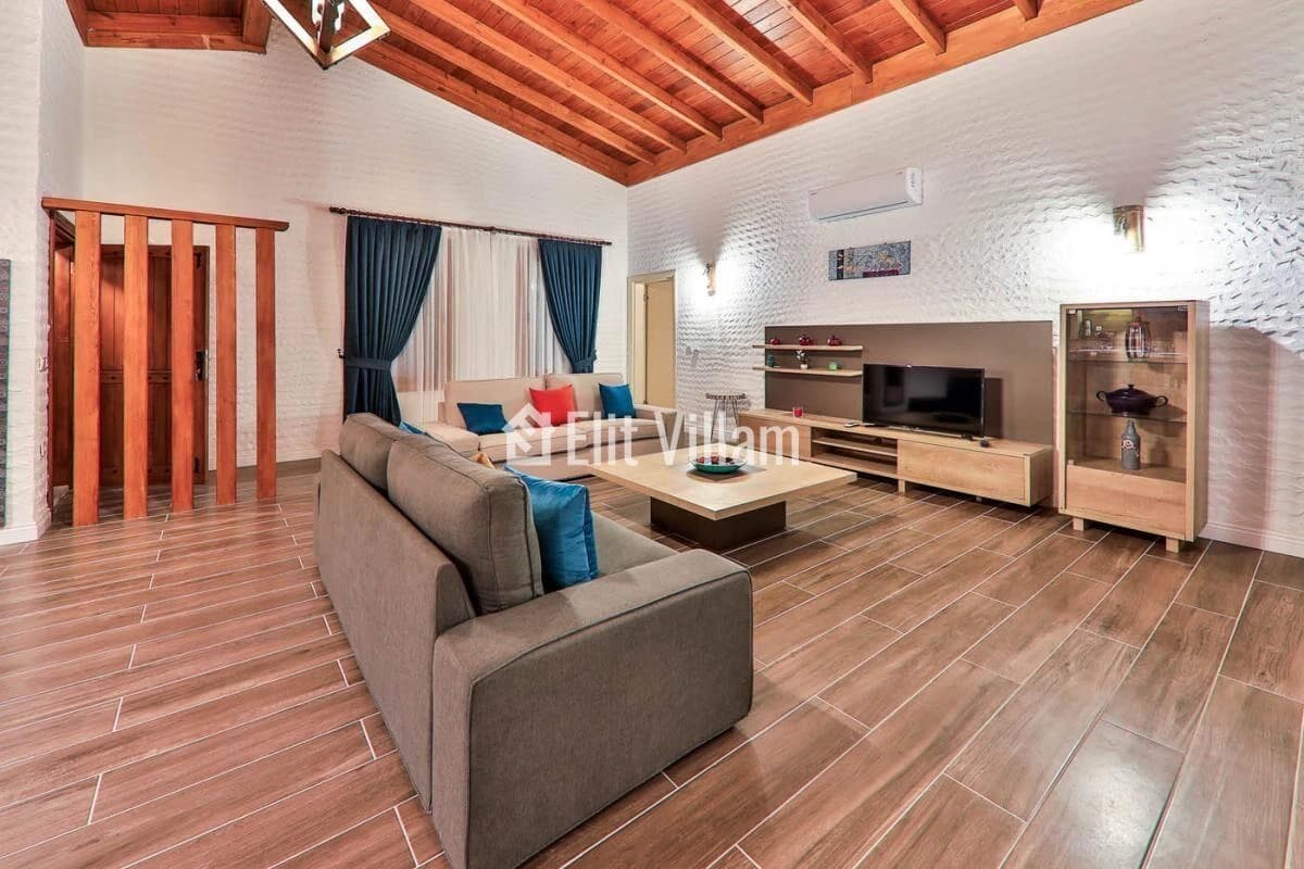 Bright living room with comfortable seating, modern TV setup, and exposed wooden ceiling.