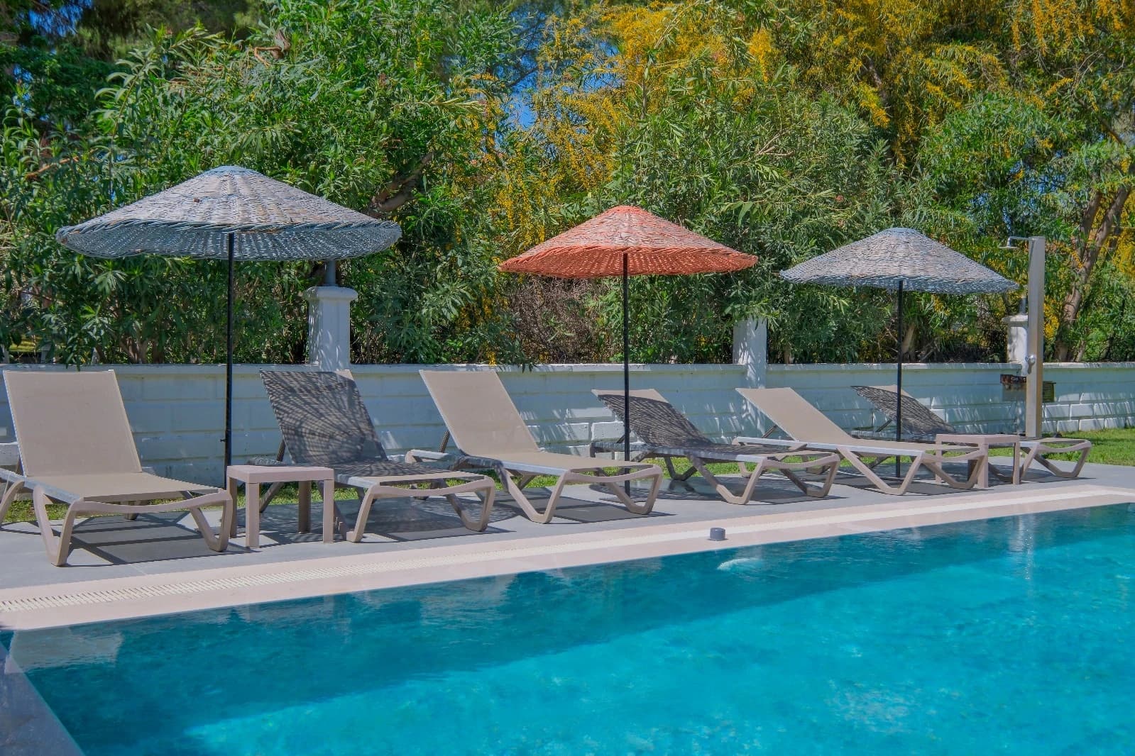 Pool area with comfortable seating, shade umbrellas, and surrounding hedges.