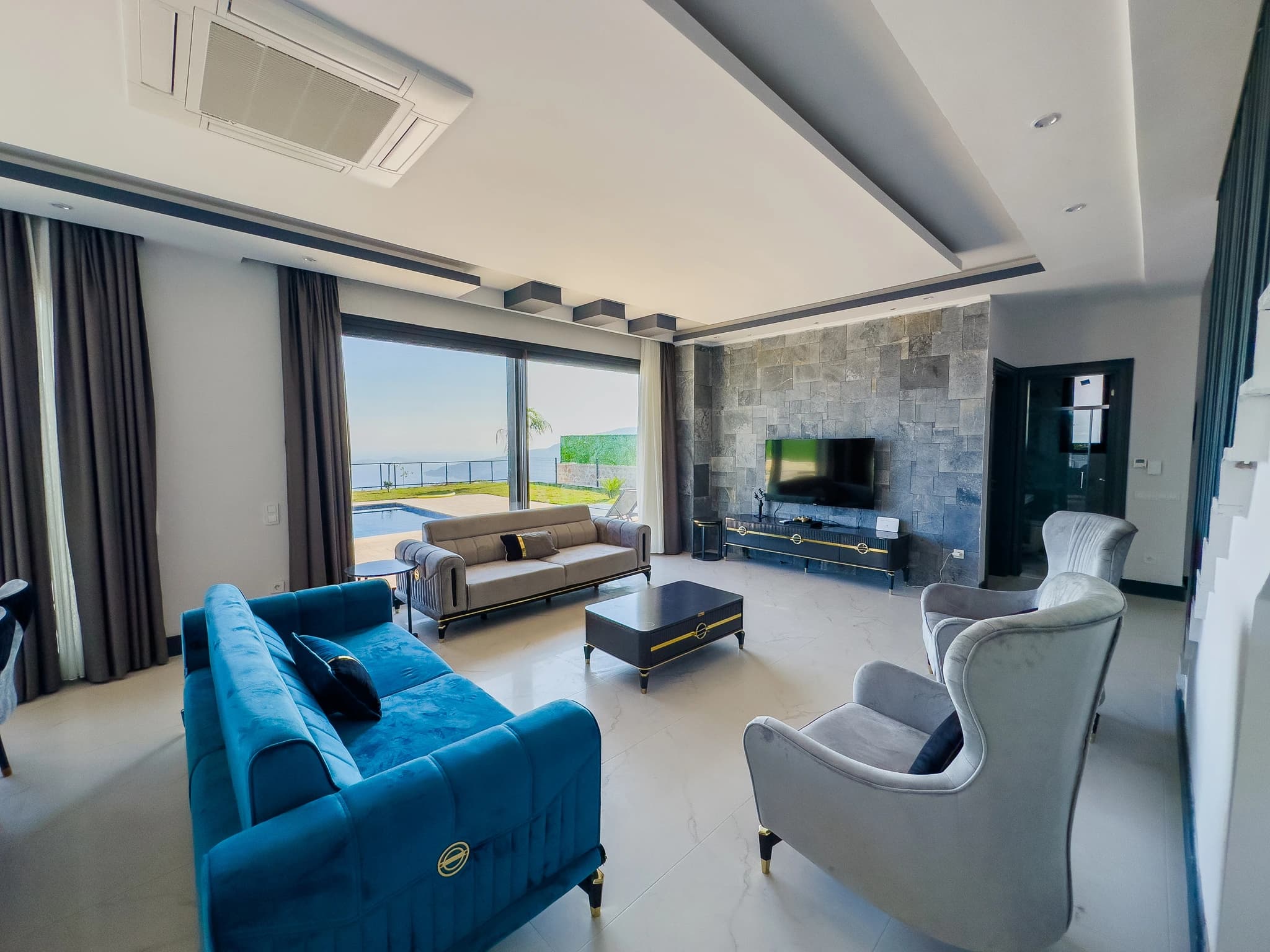 Luxury living room with stone accent wall, premium seating, and expansive sea and pool views through large windows.