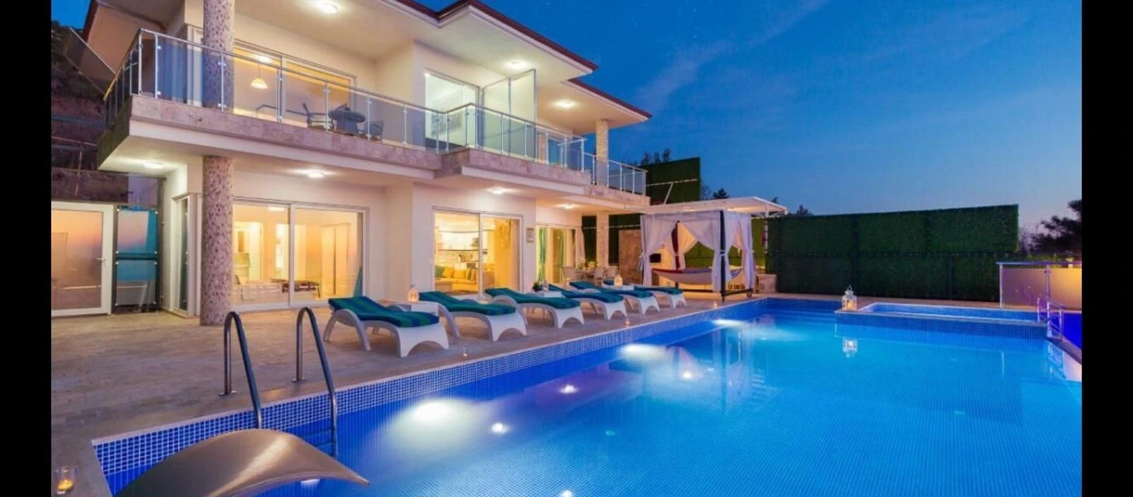 Night-time pool view showing illuminated swimming pool with loungers and modern villa.