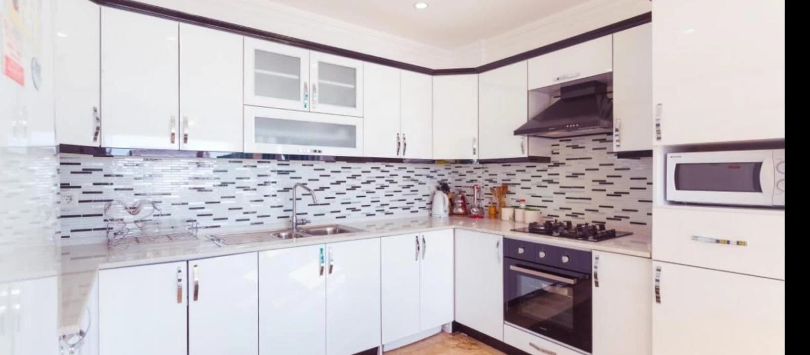 Contemporary kitchen with white cabinetry, mosaic backsplash, and integrated appliances.