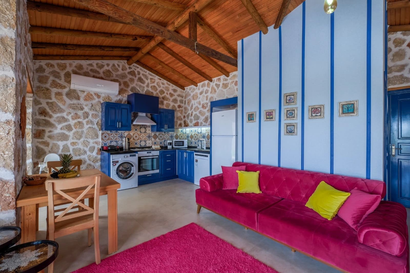 Open living space combining bedroom, kitchen, and dining with cohesive blue and magenta design.
