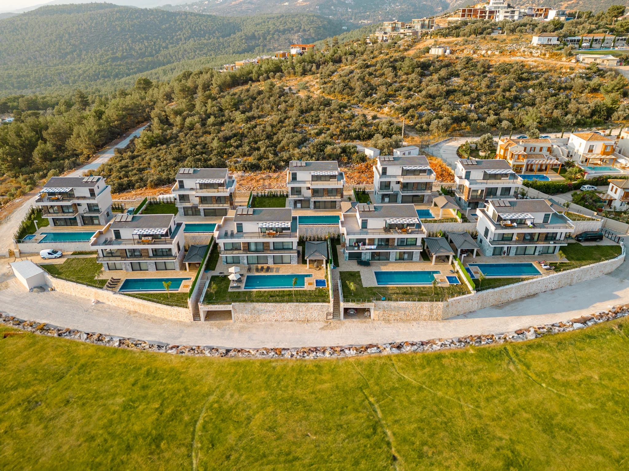 Wide aerial perspective showing the entire villa development with multiple private pools set against forested mountains.
