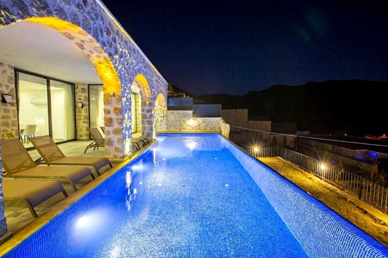 Luxurious lit infinity pool with lounge chairs and dramatic stone archways at dusk.