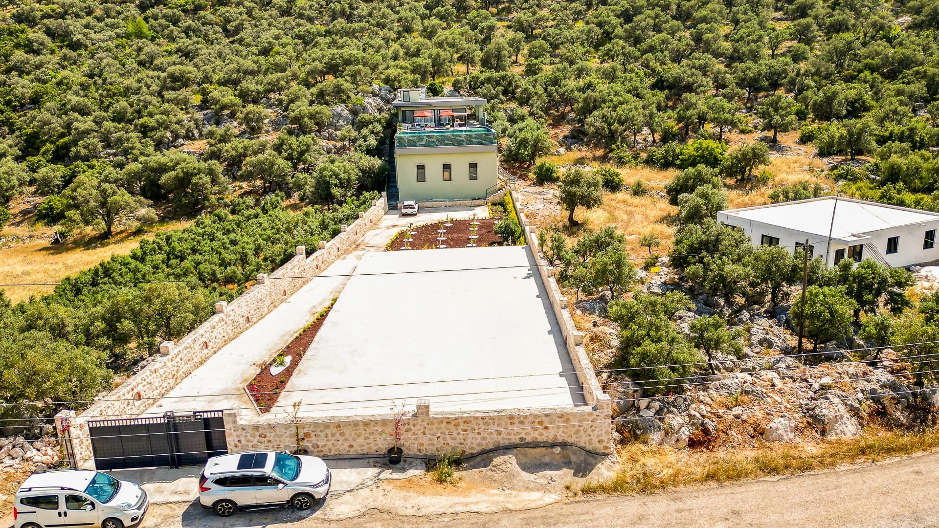 Aerial view of the contemporary villa nestled in olive groves with parking and terraced grounds.