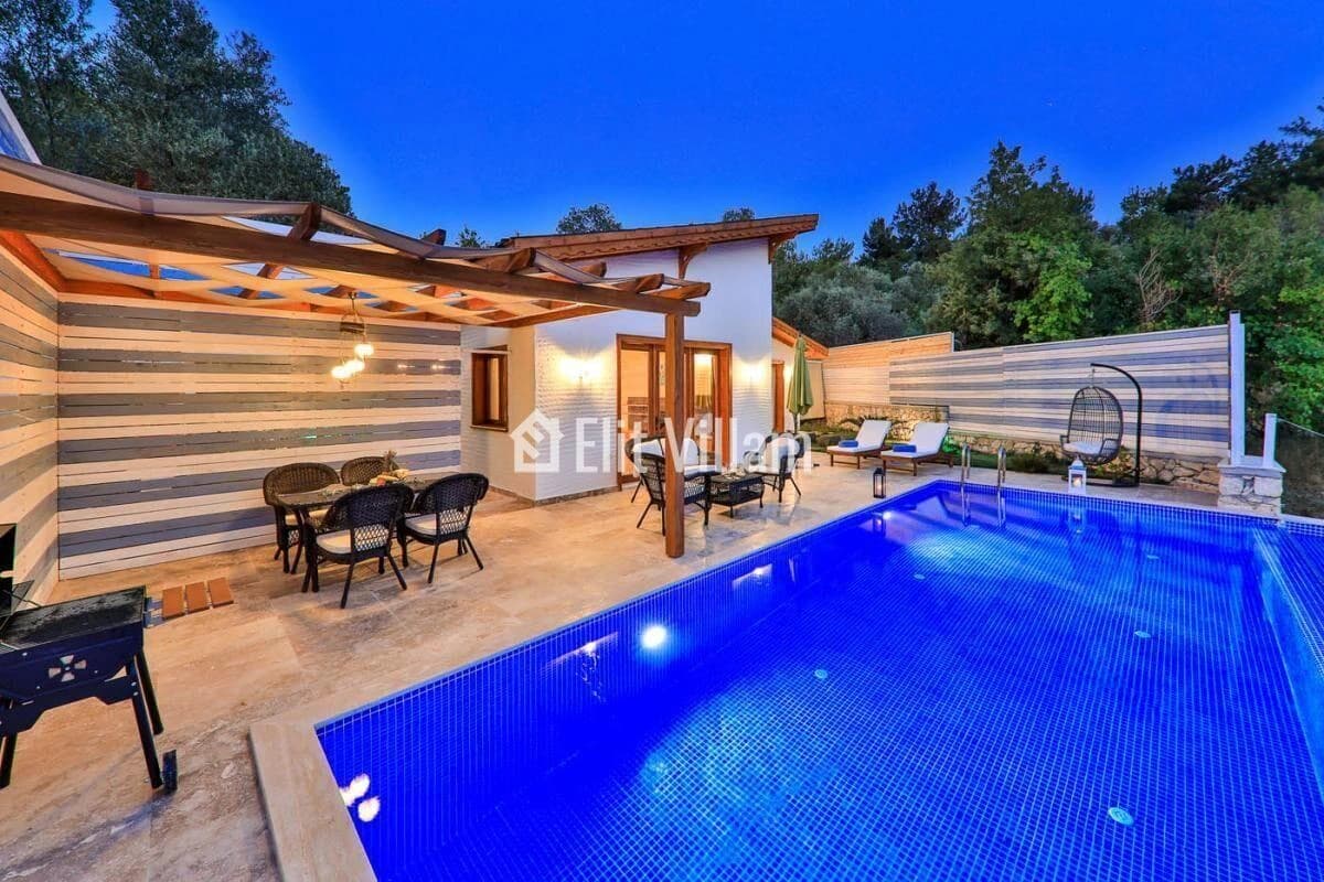 Illuminated private pool with pergola, lounge seating, and outdoor terrace at dusk.