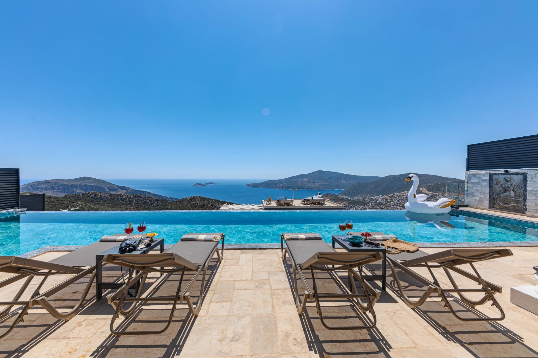Stunning infinity pool with sea and mountain views, lined with sun loungers.