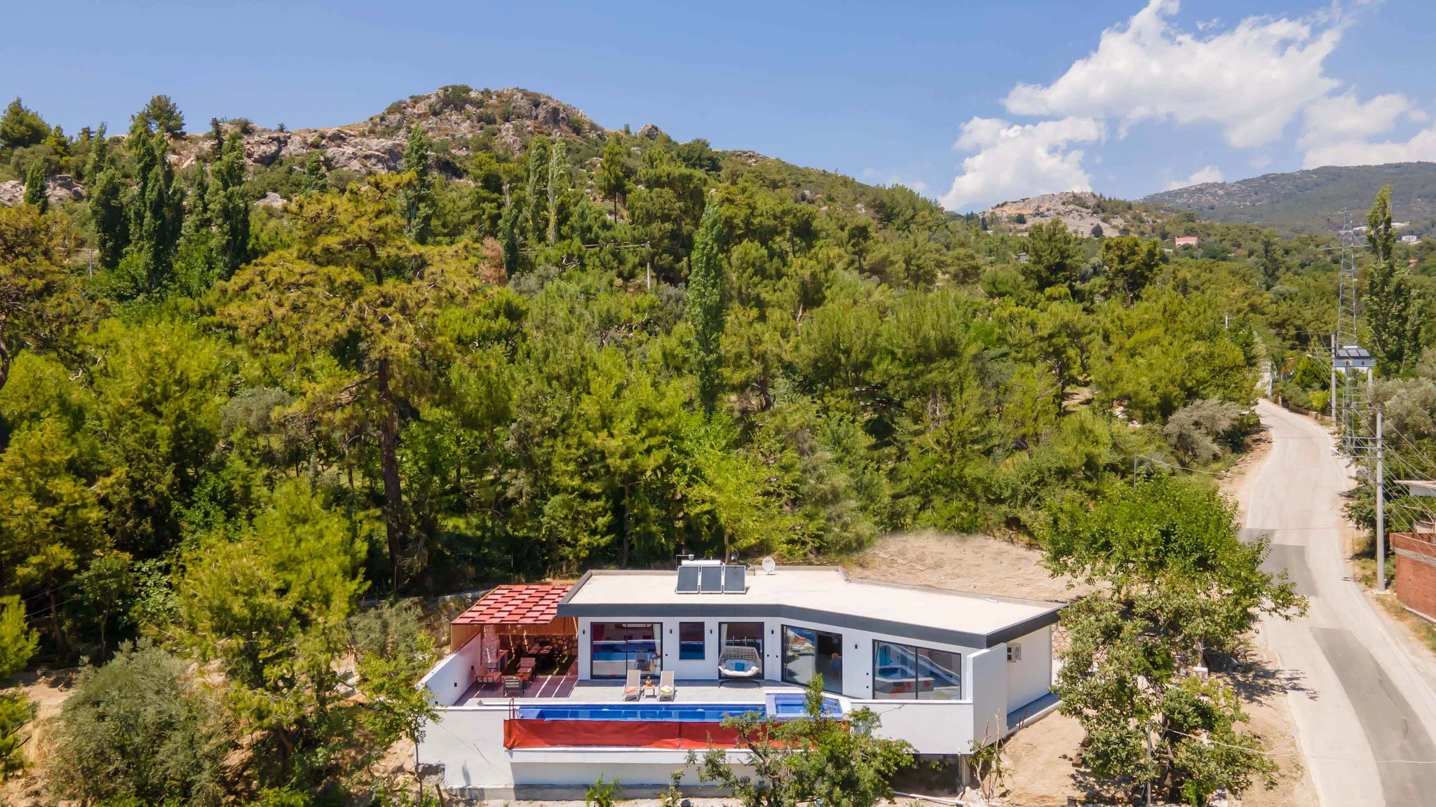 Secluded Garden Villa with Private Pool and Mountain Views in Kalkan – Contemporary villa exterior nestled in hillside forest setting with pool, red terrace canopy, and modern architecture.