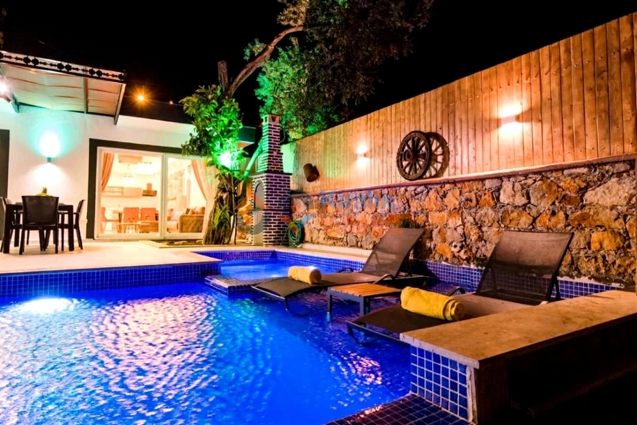 Evening pool view with rustic stone wall and elegantly positioned loungers.