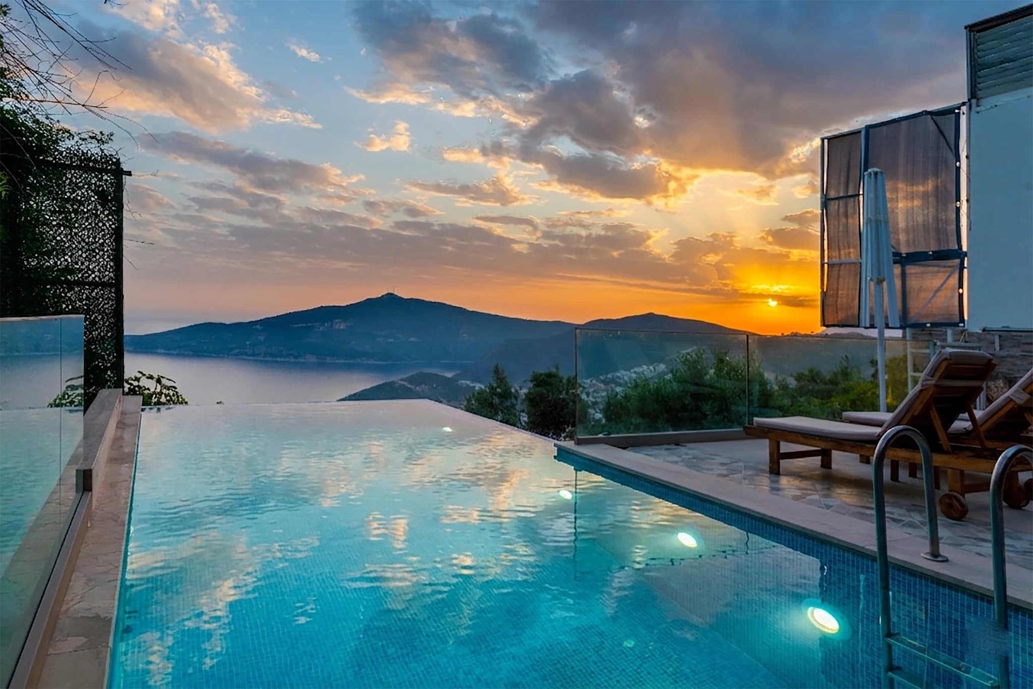 Illuminated infinity pool reflecting golden sunset with mountain backdrop.