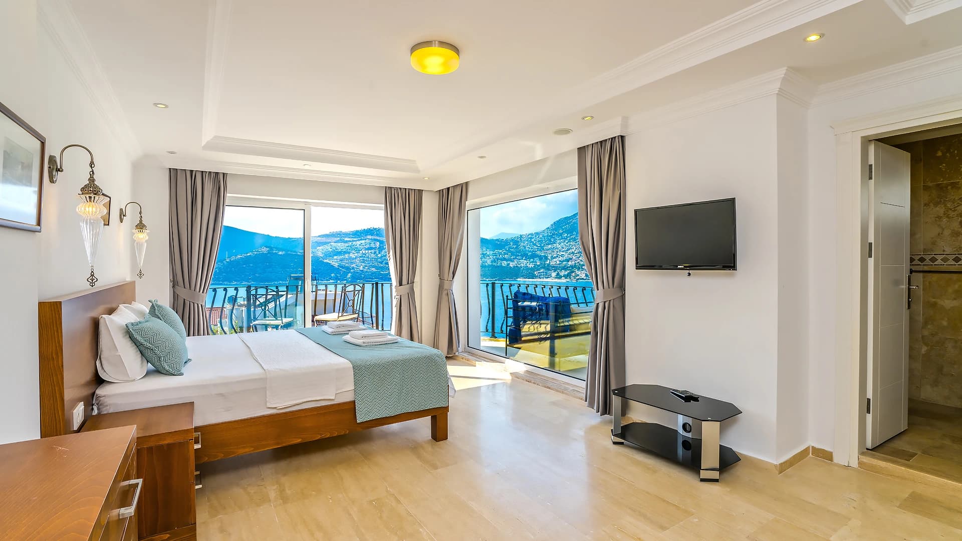 Luxurious master bedroom with panoramic sea views, modern TV, and private balcony access.