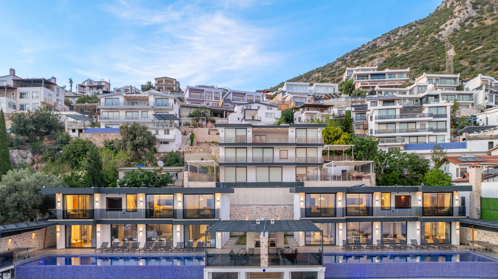 Dramatic hillside villa exterior showcasing dual pools, tiered terraces, and contemporary architectural design.
