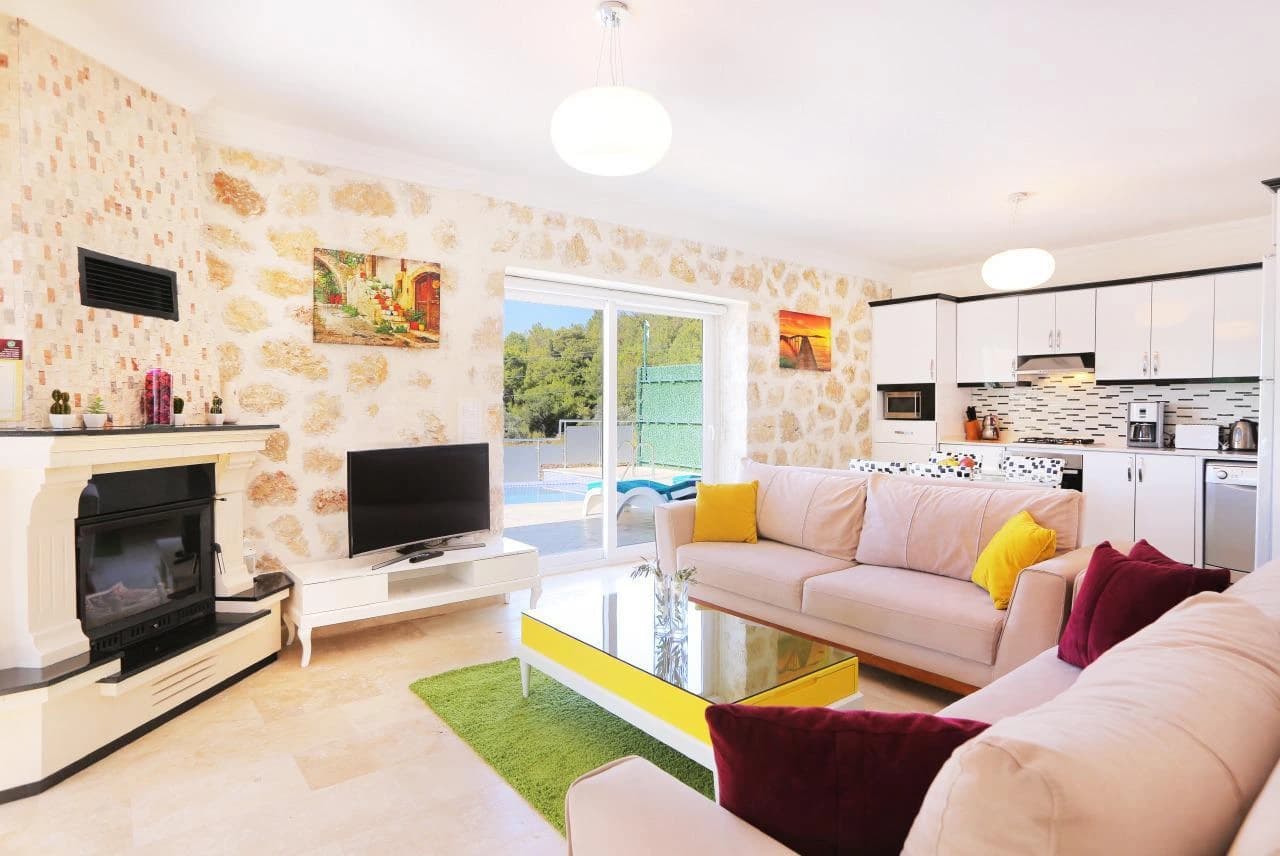 Bright open-plan living room with dual sofas, fireplace, and seamless kitchen integration.