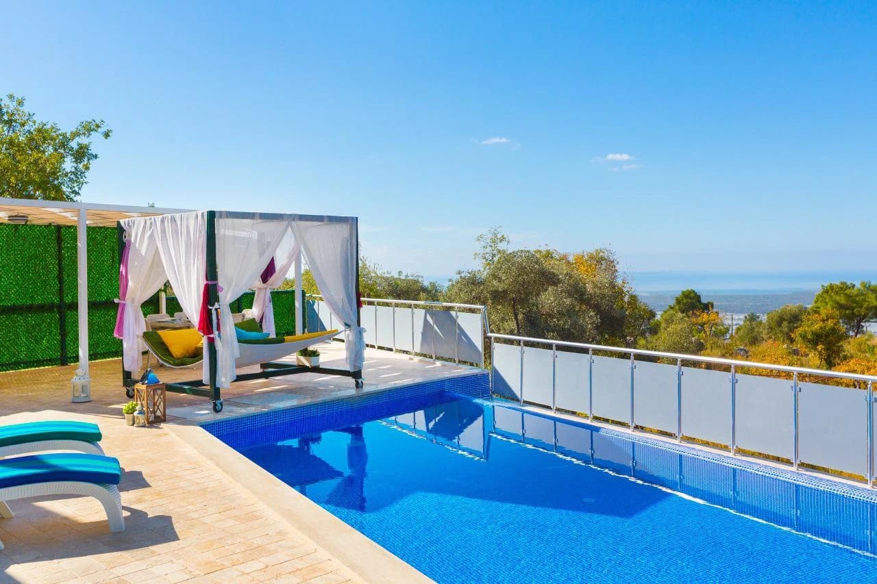 Stunning daytime pool view with loungers and a luxurious canopied daybed overlooking distant hills.