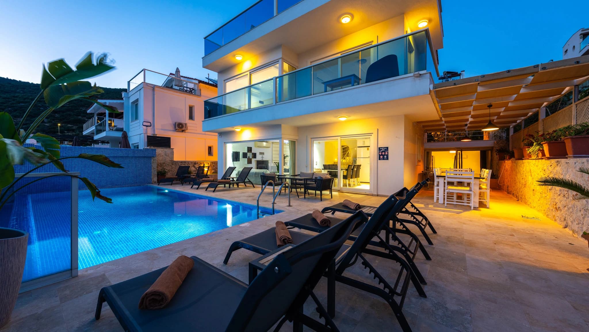 Illuminated private pool with sun loungers and modern terrace at dusk.
