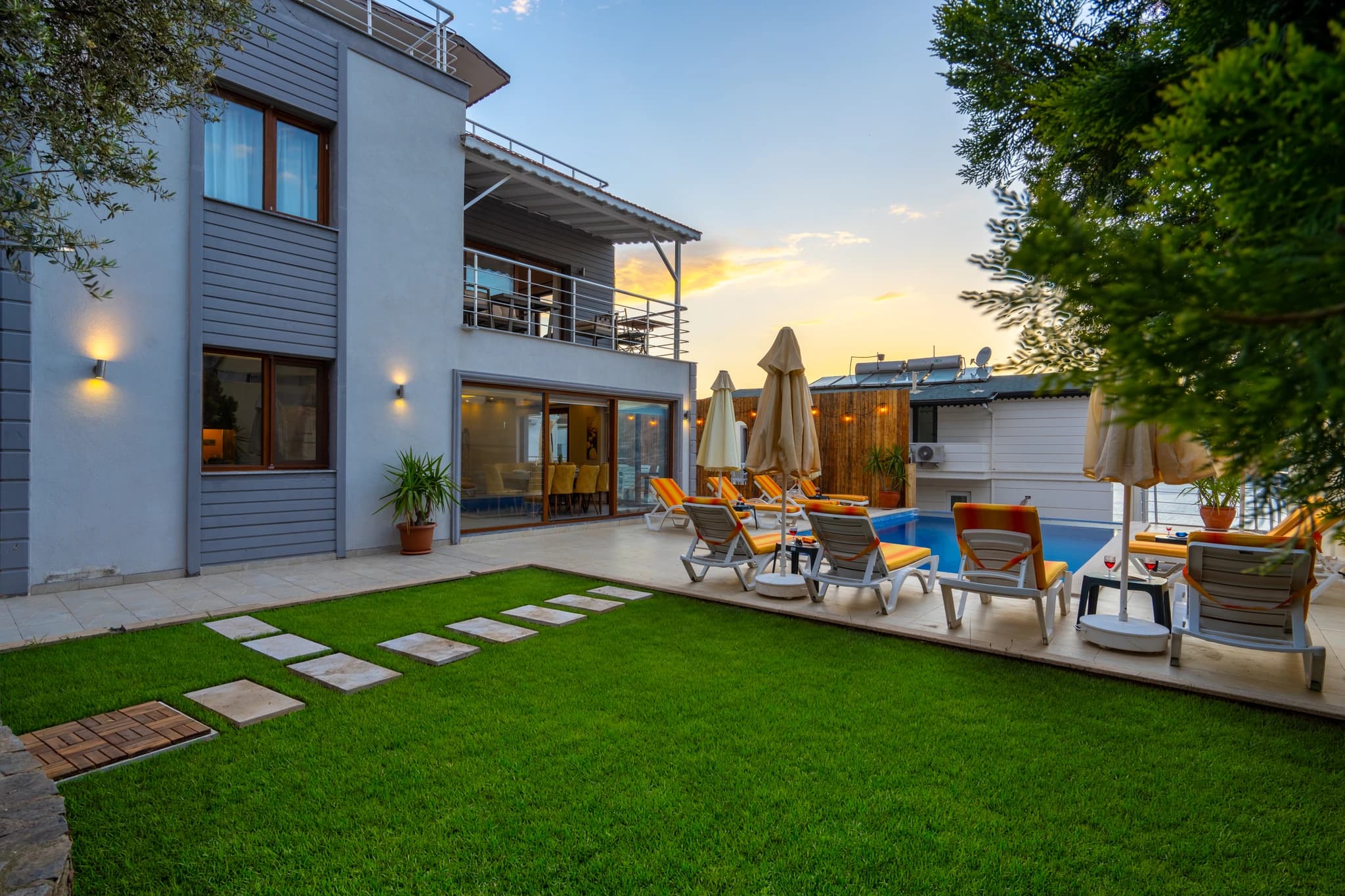 Modern villa exterior at dusk with manicured garden and poolside seating area.