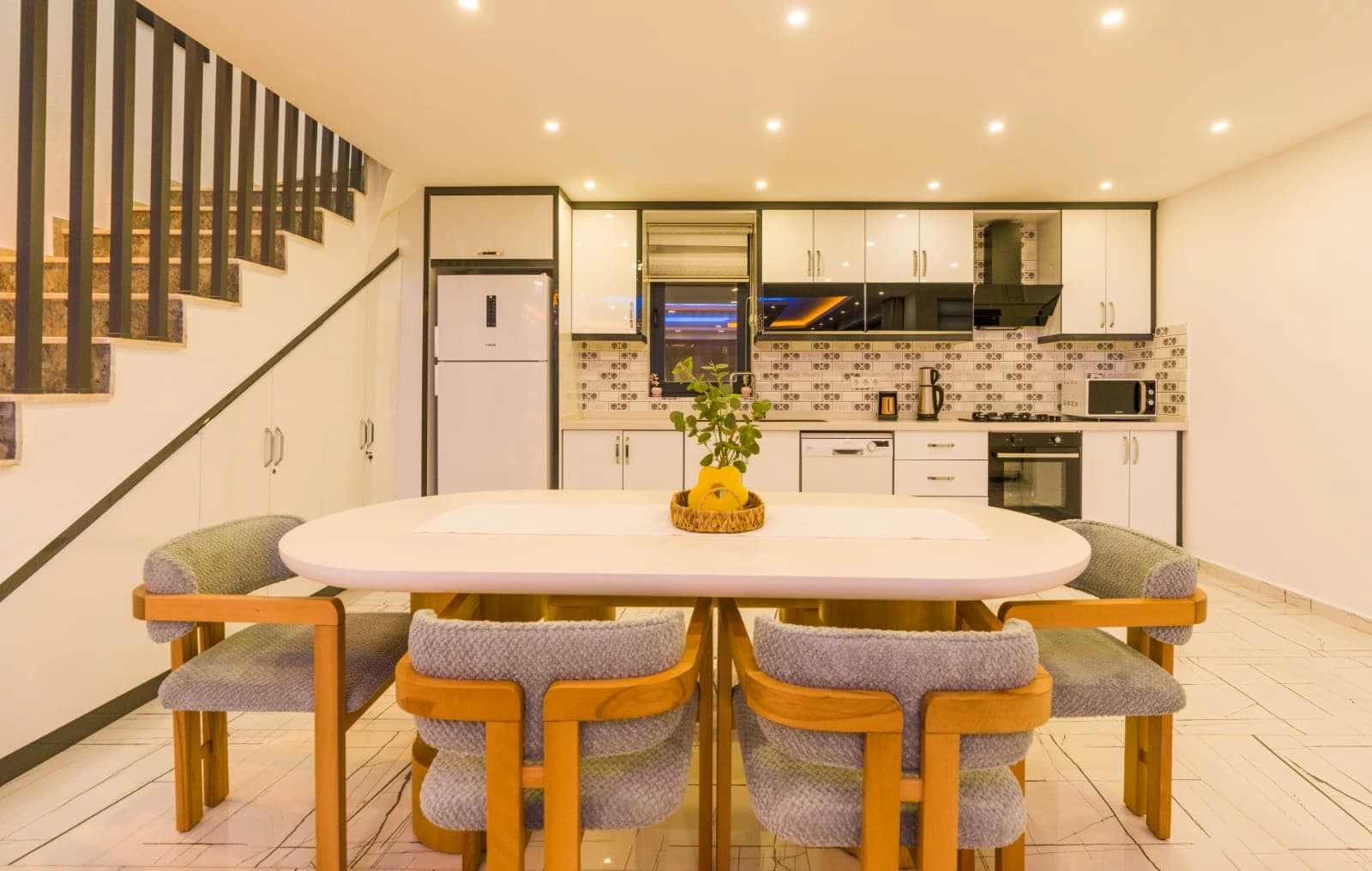 Modern dining space with oval table and integrated kitchen featuring white cabinetry.