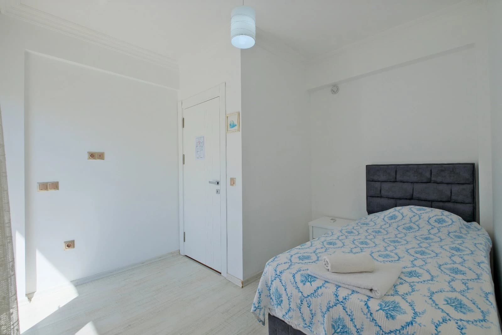 Compact bedroom with a single bed, dark headboard, and bright white walls.