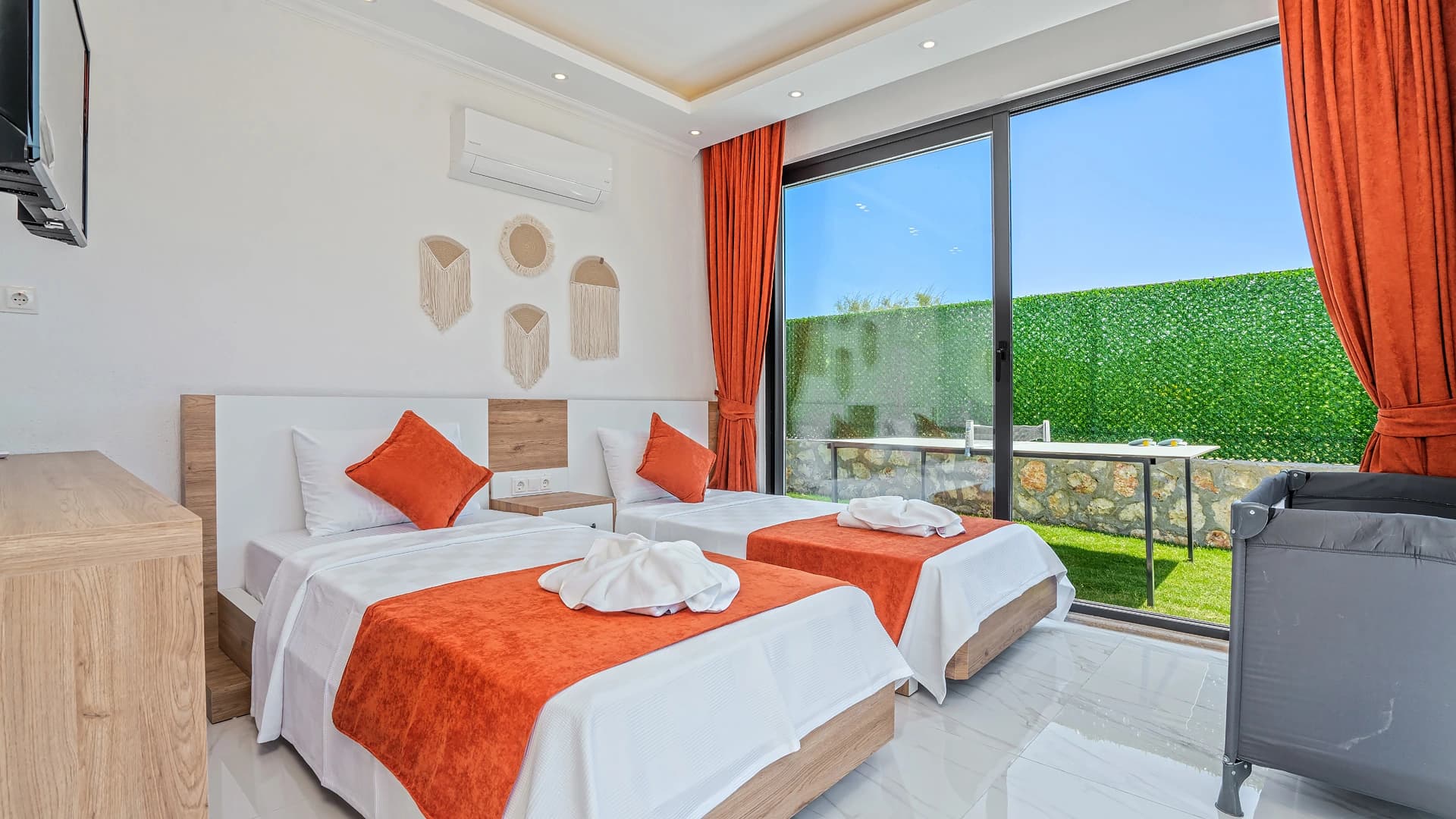 Bright modern bedroom with two twin beds, orange highlights, and stunning mountain views through sliding doors.