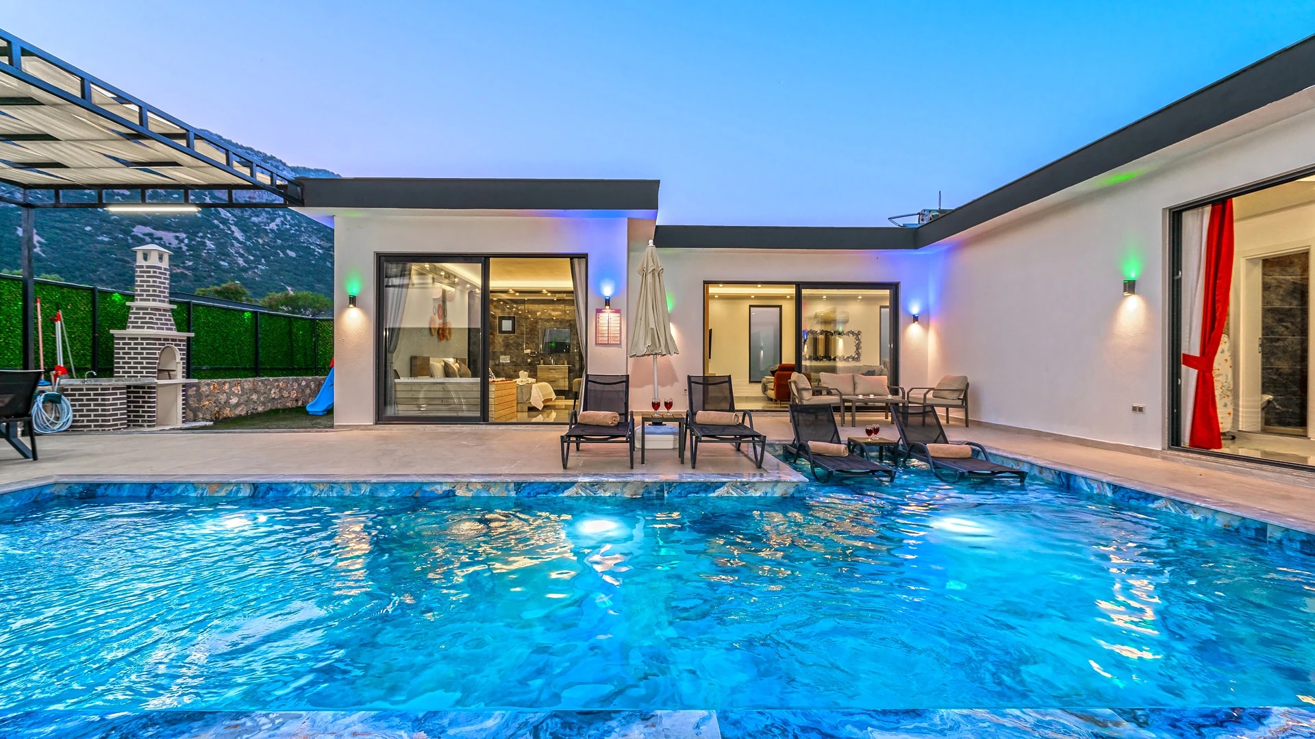 Sophisticated pool area with ambient lighting, outdoor fireplace, and covered seating.