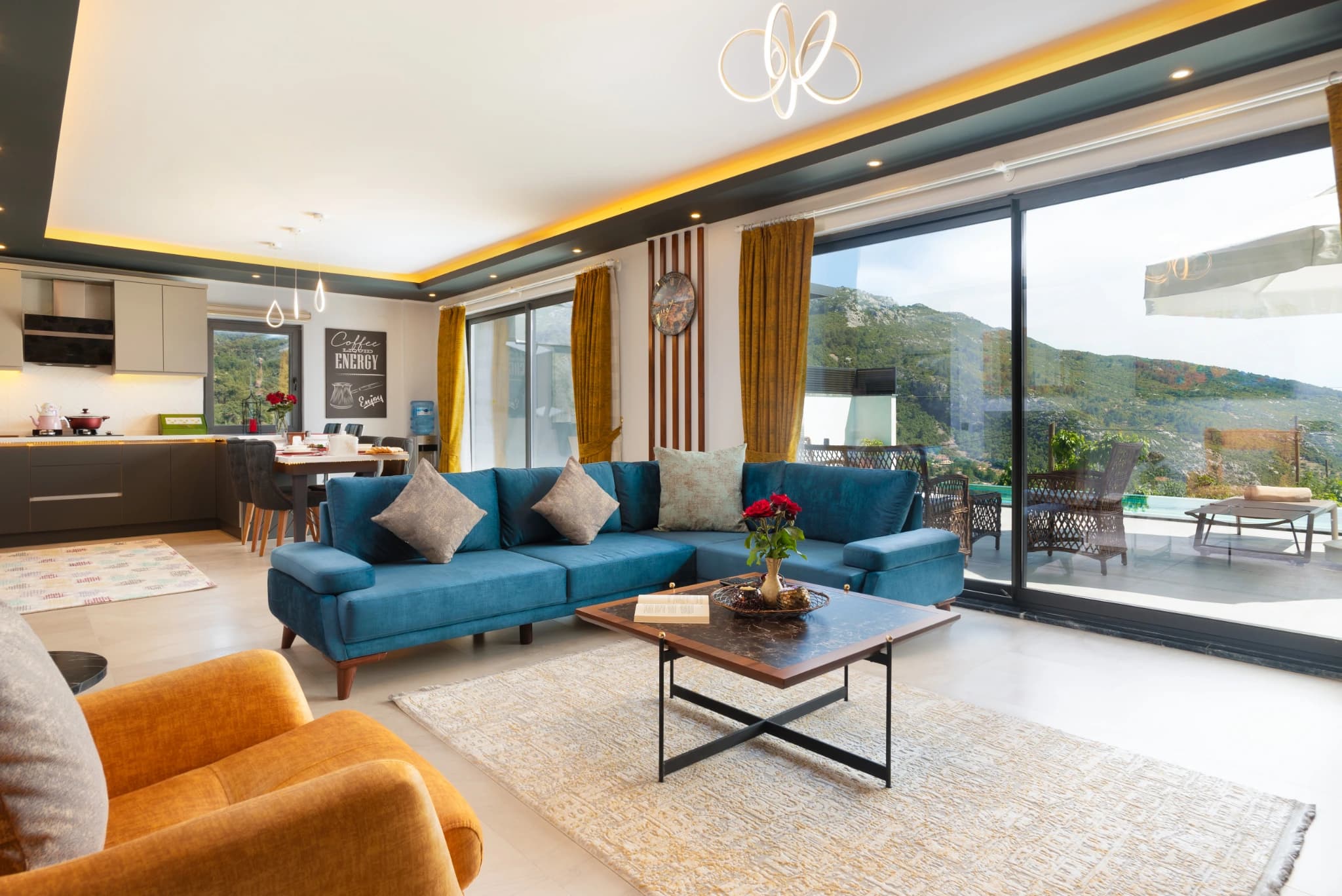 Open-plan living area with blue sectional sofa, full kitchen, and expansive mountain views.